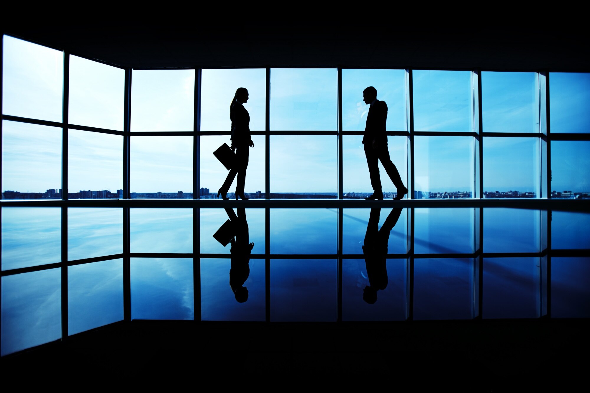 Silhouettes of two business professionals walking in a modern office with large windows