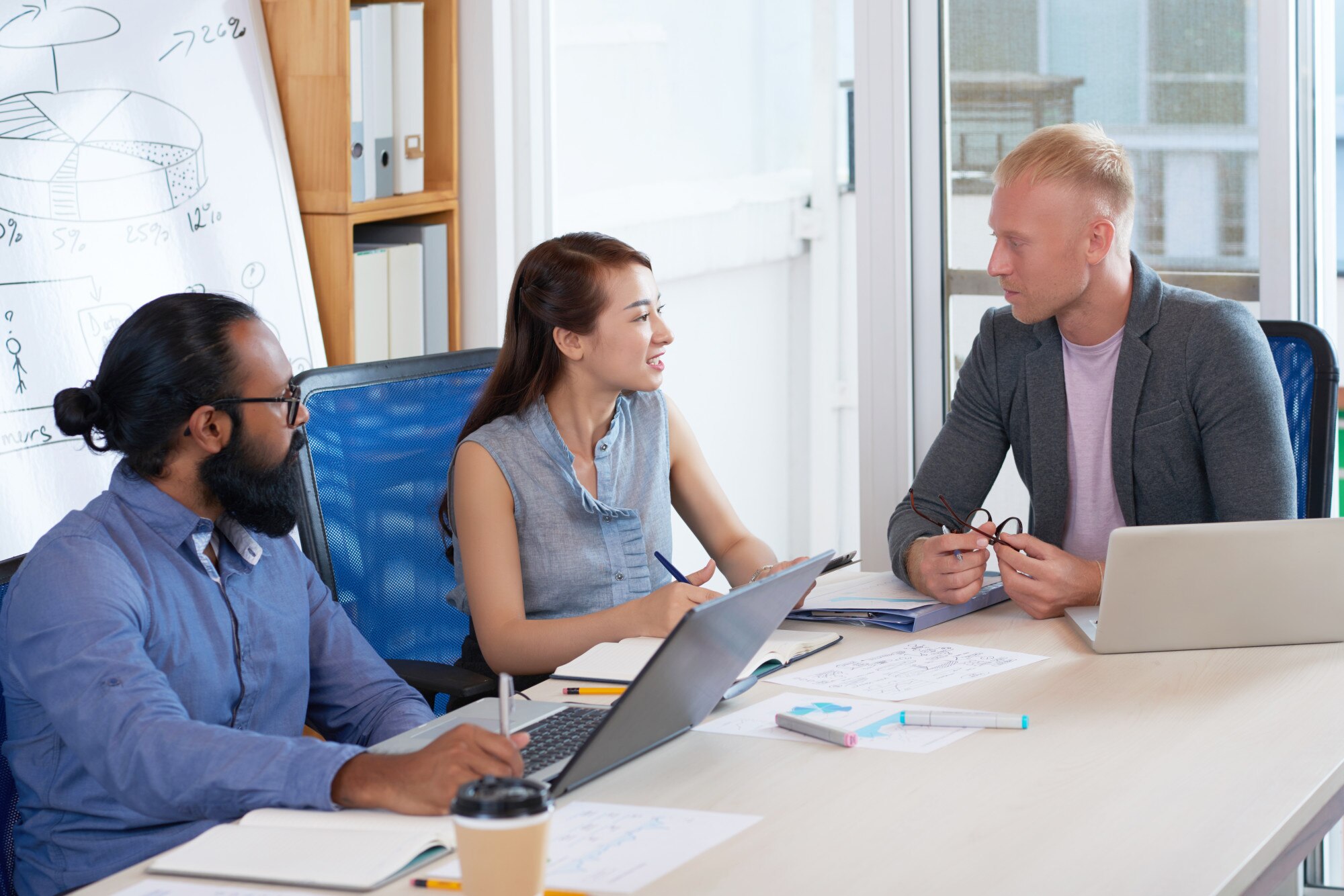 Small team collaborating at a meeting table with laptops and whiteboard